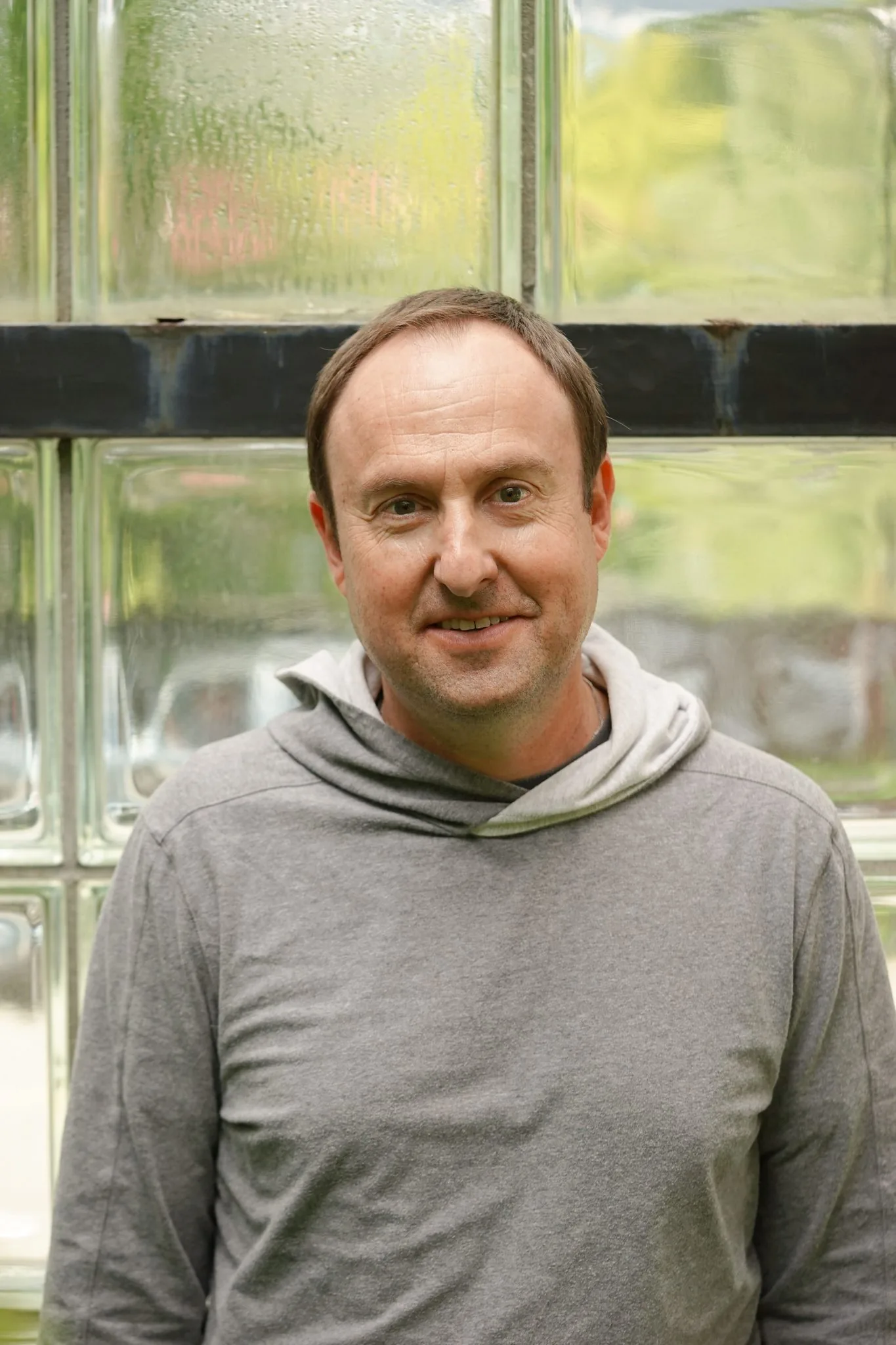 Christian G, Writing Instructor, in a grey hoodie by a glass-block wall